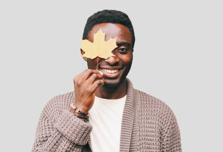 Portrait of happy smiling african man with autumn yellow maple leaves on a gray backgroundの写真素材