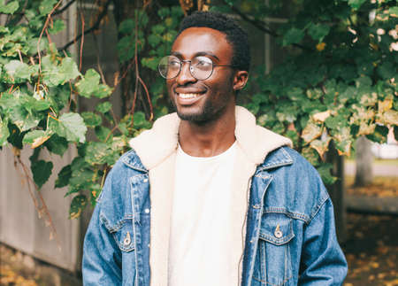 Portrait of happy smiling african man looking away wearing an eyeglasses in autumn city parkの写真素材