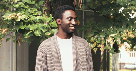 Portrait of happy smiling african man looking away in autumn city parkの写真素材