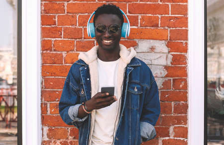 Portrait of happy smiling young african man with smartphone listening to music on city streetの写真素材