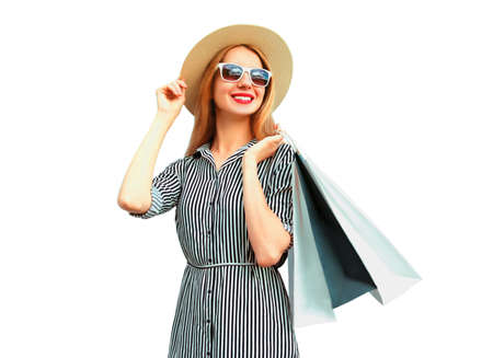Portrait of happy smiling young woman with shopping bags wearing summer straw round hat, black white striped dress isolated on white backgroundの写真素材