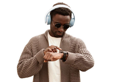 Portrait of african man in headphones looking at smart watch using voice assistant or takes calling while listening to music isolated on white backgroundの写真素材