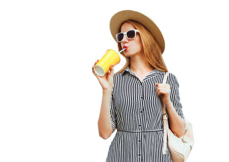 Portrait of beautiful young woman drinking fruit juice wearing summer round straw hat, striped dress isolated on white backgroundの写真素材