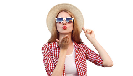 Portrait of beautiful young woman blowing her red lips sending sweet air kiss wearing a summer straw hat isolated on white backgroundの写真素材