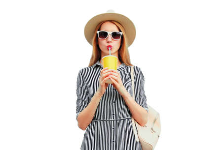 Portrait of beautiful young woman drinking fruit juice wearing summer round straw hat, striped dress isolated on white backgroundの写真素材