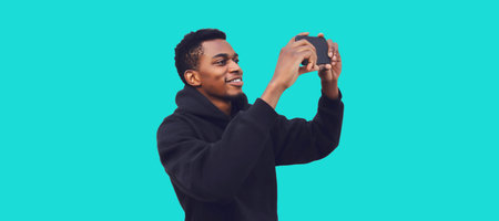 Portrait of happy smiling young african man taking selfie by smartphone isolated on blue background