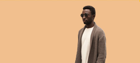 Portrait of stylish young african man model looking away wearing knitted cardigan isolated on brown background, blank copy space for advertising textの写真素材