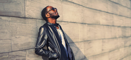 Portrait of stylish young african man wearing black rock leather jacket on city street backgroundの写真素材