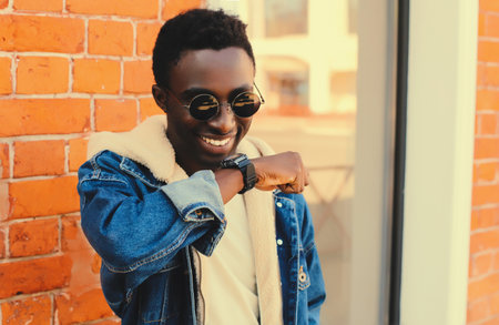 Portrait of stylish happy smiling african man with smart watch using voice command recorder or takes calling on city streetの写真素材