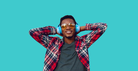 Portrait of happy smiling african man listening to music in wireless headphones isolated on blue...
