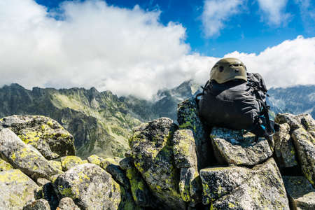 Black backpack with helmet on the summit and clouds over the ridge.の写真素材