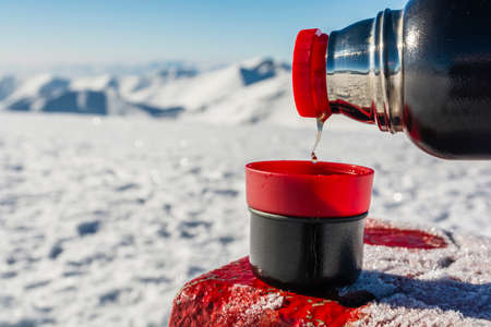 Pouring hot tea from a thermos into a cup in the winter in the mountains.の写真素材