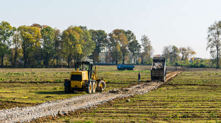Niedomice, Poland - October 19, 2017: Construction site. A truck crushing the aggregate on the road foundation. The grader waits to level the supplied material.のeditorial素材