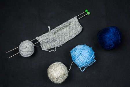 Three different colored balls of wool and the start of a manual knit on a dark background.の写真素材