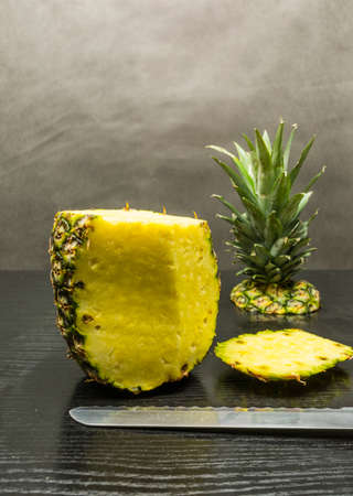 A ripe pineapple fruit while peeling with a knife on a wooden table.の写真素材