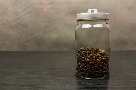 Delicious coffee beans are standing in a jar on a dark wooden table.の写真素材