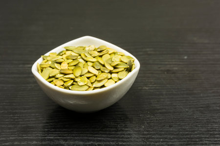 White bowl with pumpkin seeds on a dark table.