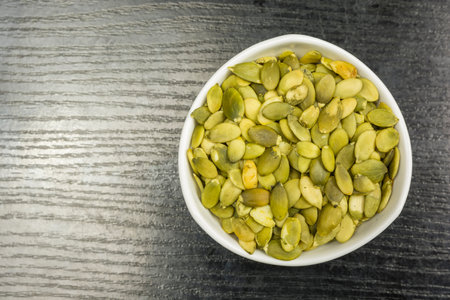 White bowl with pumpkin seeds on a dark table. View from above.