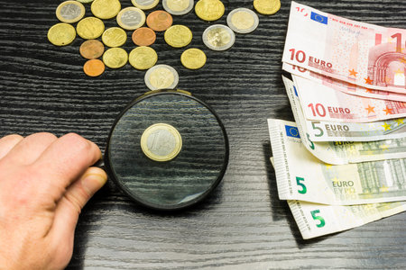 Money on the table. One euro coin enlarged by a magnifying glass.の写真素材