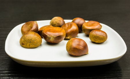 Ripe edible chestnuts on a white plate on a wooden table.
