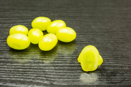 Cut white grape on a wooden table and a few whole fruits in the background.