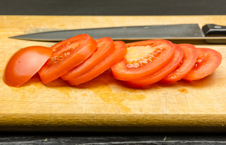Ripe red tomato cut with a knife on slices on a wooden chopping board.の写真素材