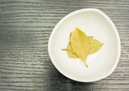 Dried bay leaves in a porcelain bowl on a wooden table.の写真素材
