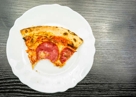 A bitten portion of pepperoni pizza on a plate on a wooden table. View from above.の写真素材