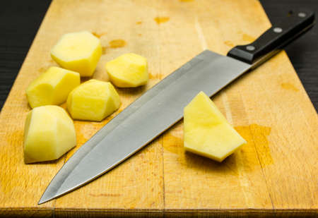 Peeled raw potatoes prepared for cutting with a knife on a chopping board.の写真素材