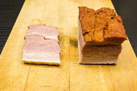 Two sliced bacon slices on a wooden chopping board.の写真素材