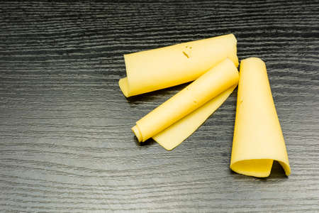 Yellow cheese rolled into rolls on a dark basis.の写真素材