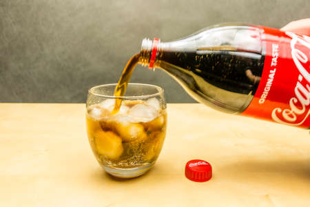 Niedomice, Poland - March 09, 2018: Pouring Coca-Cola from a bottle into a glass with ice cubes.のeditorial素材
