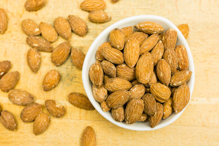 Raw shelled almond seeds in a bowl on a wooden base, on which they are also sprinkled.. View from above.の写真素材