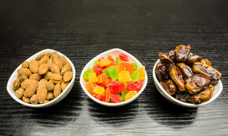 White bowls with additives for cakes and desserts: dried dates, colored cubes of candied pineapple and shelled almonds.の写真素材