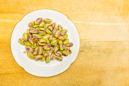 A white plate with shelled, roasted pistachios on a wooden background. View from above.の写真素材
