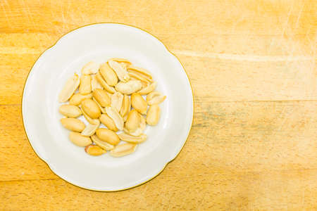 A white plate with shelled peanuts on a wooden background. View from above.の写真素材
