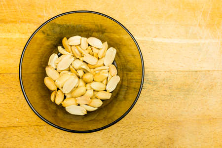 Bowl with shelled peanuts on a wooden background. View from above.の写真素材