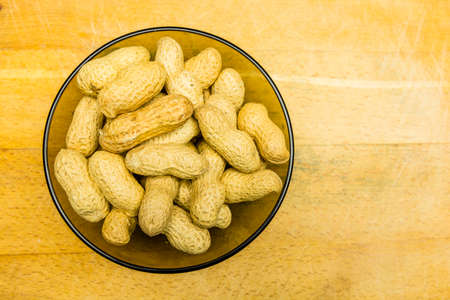 Bowl with unshelled peanuts on a wooden background. View from above.の写真素材