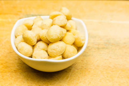 Bowl with roasted and salted macadamia nuts on a wooden background.の写真素材