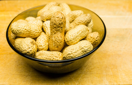 Bowl with unshelled peanuts on a wooden background.