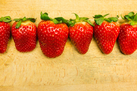 A row of ripe red strawberries on a wooden board.の写真素材
