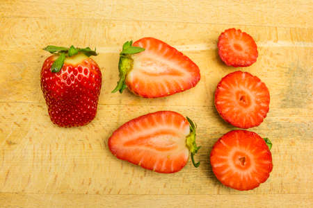 Whole and different cross-section of red ripe strawberries on a wooden board.の写真素材
