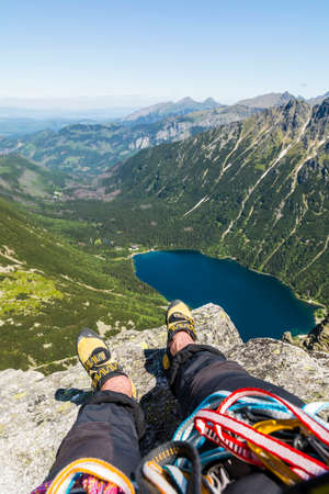 Climbing shoes on the feet of a climber during a rest at the top after climbing. View from Mnich to Lake Morskie Oko and surrounding Tatra Mountains peaks.の写真素材