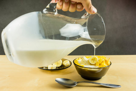Fast and nutritious breakfast good for children and adults. Pouring cold milk from the jug into a...