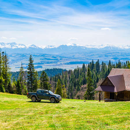 Nowy Targ, Poland - April 24, 2020: Mitsubishi L200 Warrior - A car parked in a clearing in the woods next to a wooden house in the mountains. In the background visible snowy mountains - Tatras.のeditorial素材