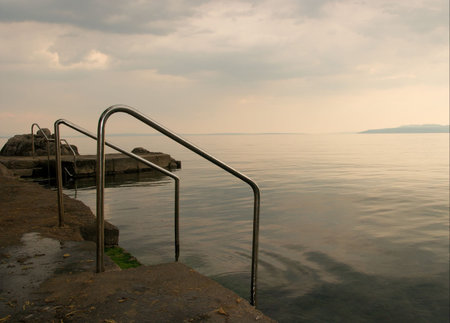 Rocks sea shore, overcast sky, stairs into the waterの写真素材