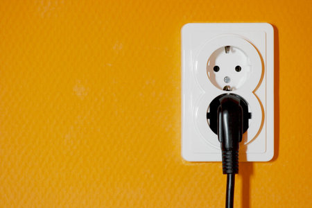 Electric socket with a connected plug on orange wall