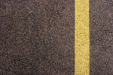 Texture closeup of an asphalt road with painted yellow line on the sideの写真素材