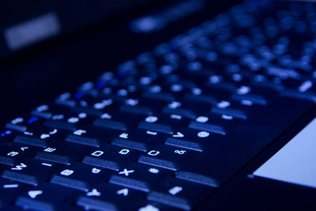 Keyboard of a laptop illuminated with blue light in the dark
