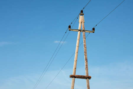 Old wooden electric pillar against blue skyの写真素材